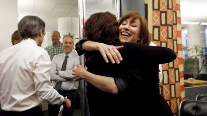 Woman happily hugging another woman while men smile in the background