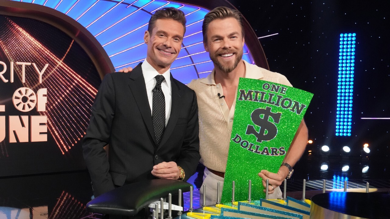 RYAN SEACREST and DEREK HOUGH side by side smiling on the set of Wheel of Fortune.