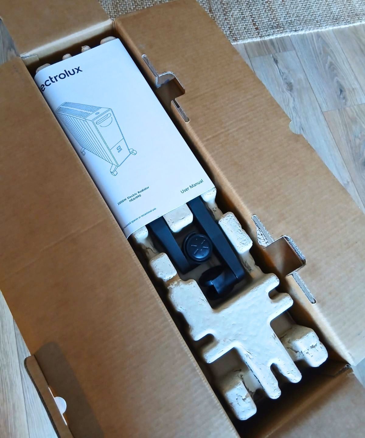 Open cardboard box showing an Electrolux heater's user manual and black wheel legs in moulded packaging.