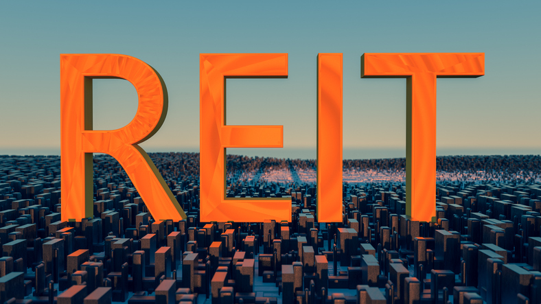 Business acronym REIT, short for real estate investment trust, in orange over a cityscape.