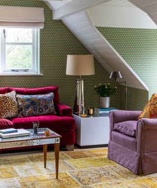 A green sitting room with colorful sofas and a wood and mirrored coffee table sat on a patchwork yellow rug