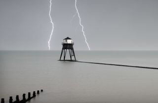 Heritage Counts 2019 – The Dovercourt Lighthouses and Causeway, Marine Parade, Dovercourt, Harwich, Essex. General view of the outer lighthouse with stormy sky and lightening, commissioned by Trinity House with work commencing in 1862 and completion in 1863. Designed with four massive tubular legs (arranged in `V'shaped pairs) to support an octagonal superstructure. The access stairs also terminate with a gate some 2m from the base, but are less elaborate than those of the inner light, reaching the doorway on the southern side in a single flight. The construction of the two storey superstructure is comparable to the inner lighthouse, with matching internal stairs, balcony, window casements and lamp aperture. A single short chimney pipe protrudes from the centre of the leaded canopy roof.