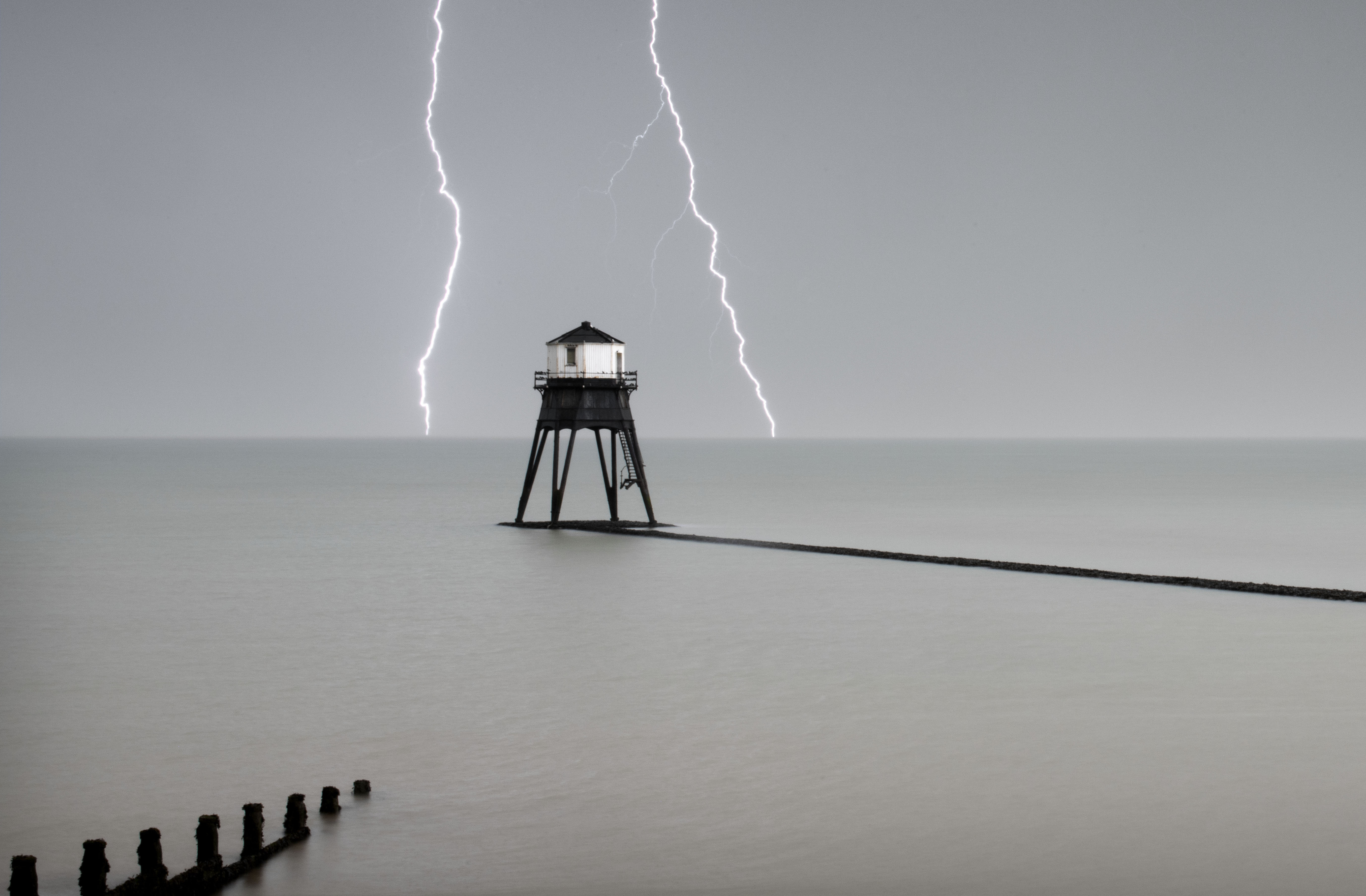 Heritage Counts 2019 – The Dovercourt Lighthouses and Causeway, Marine Parade, Dovercourt, Harwich, Essex. General view of the outer lighthouse with stormy sky and lightening, commissioned by Trinity House with work commencing in 1862 and completion in 1863. Designed with four massive tubular legs (arranged in `V&#039;shaped pairs) to support an octagonal superstructure. The access stairs also terminate with a gate some 2m from the base, but are less elaborate than those of the inner light, reaching the doorway on the southern side in a single flight. The construction of the two storey superstructure is comparable to the inner lighthouse, with matching internal stairs, balcony, window casements and lamp aperture. A single short chimney pipe protrudes from the centre of the leaded canopy roof.