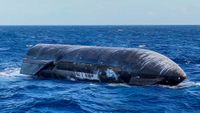 a large black cylinder with wing-like canards floats on top of a choppy blue sea