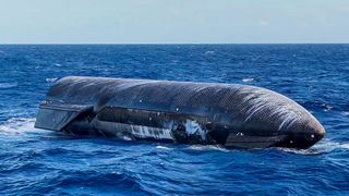 a large black cylinder with wing-like canards floats on top of a choppy blue sea