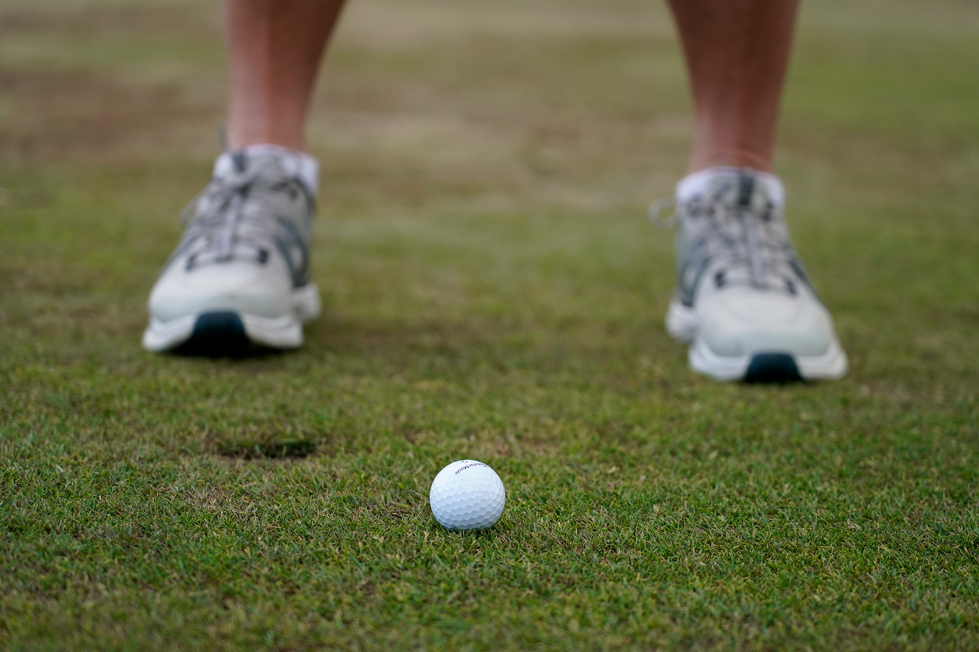 A golfer&#039;s ankles and feet in front of a brand new golf ball sitting on the fairway