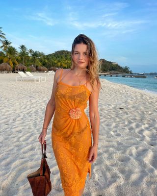 Woman wearing black bikini and orange lace dress on the beach