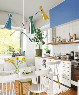 Mid-century inspired kitchen with blue colour block wall, multi-coloured ceiling pendant and fresh flowers