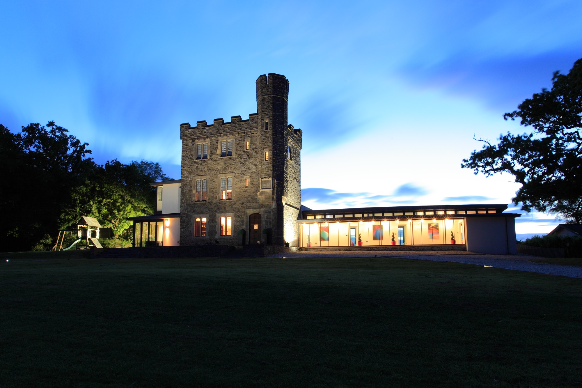 Exterior view of the listed hunting lodge with brightly lit glass extension at night