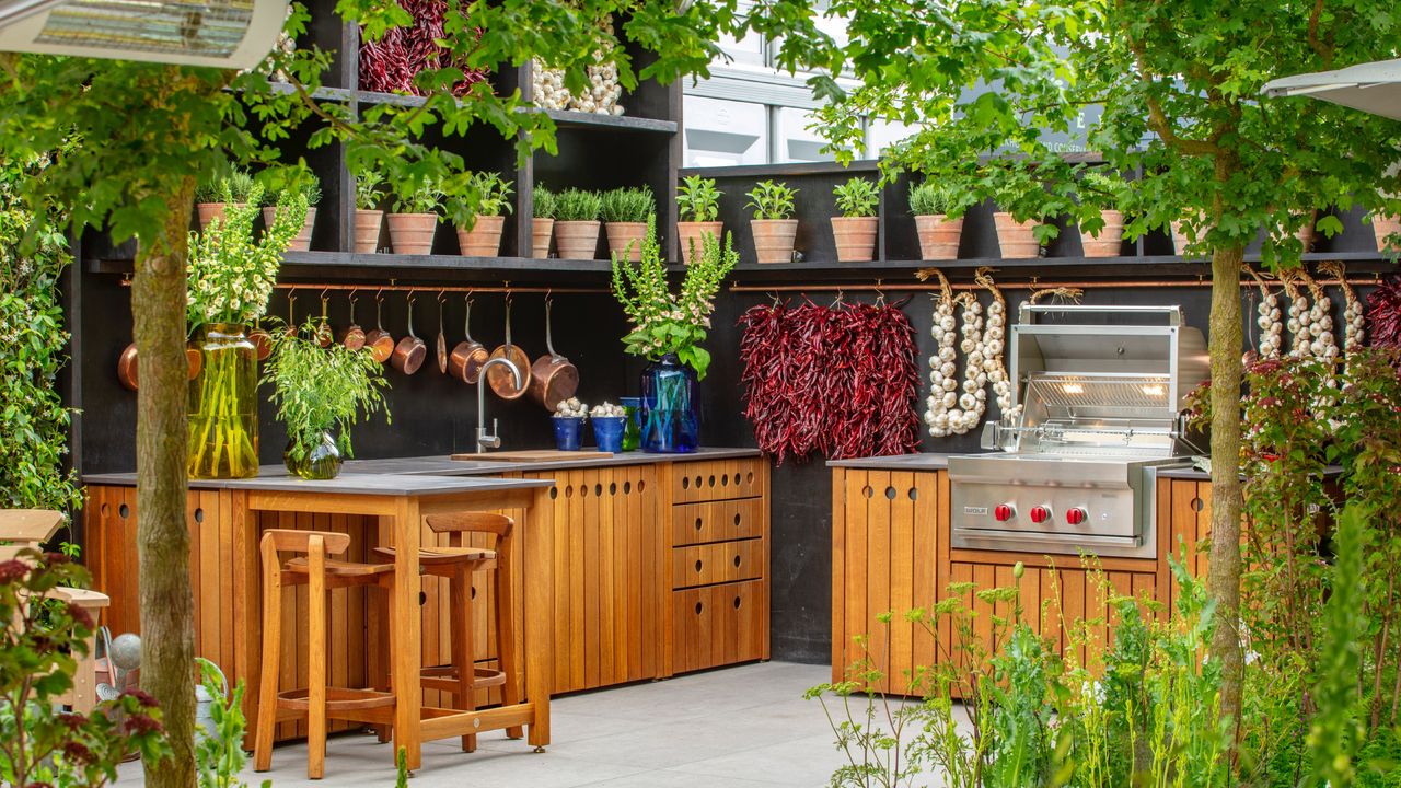 custom built outdoor kitchen with sink, storage, herbs, stone tiled floor, vases of flowers, BBQ