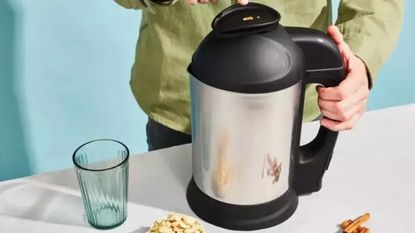 Almond Cow Milk Maker on a countertop with a blue wall and man in the background