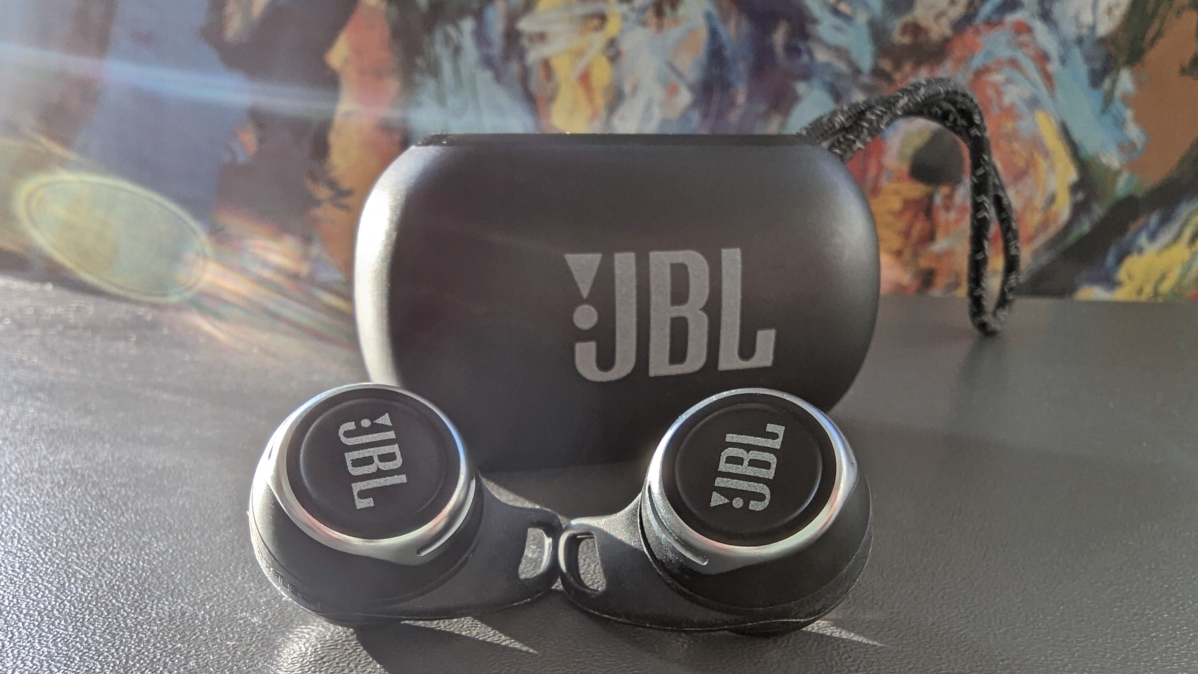 JBL Reflect Flow Pro ligger på et bord med etuiet og et kulørt maleri i baggrunden