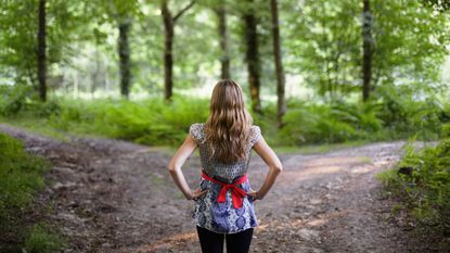 A woman stands before two paths through the woods.