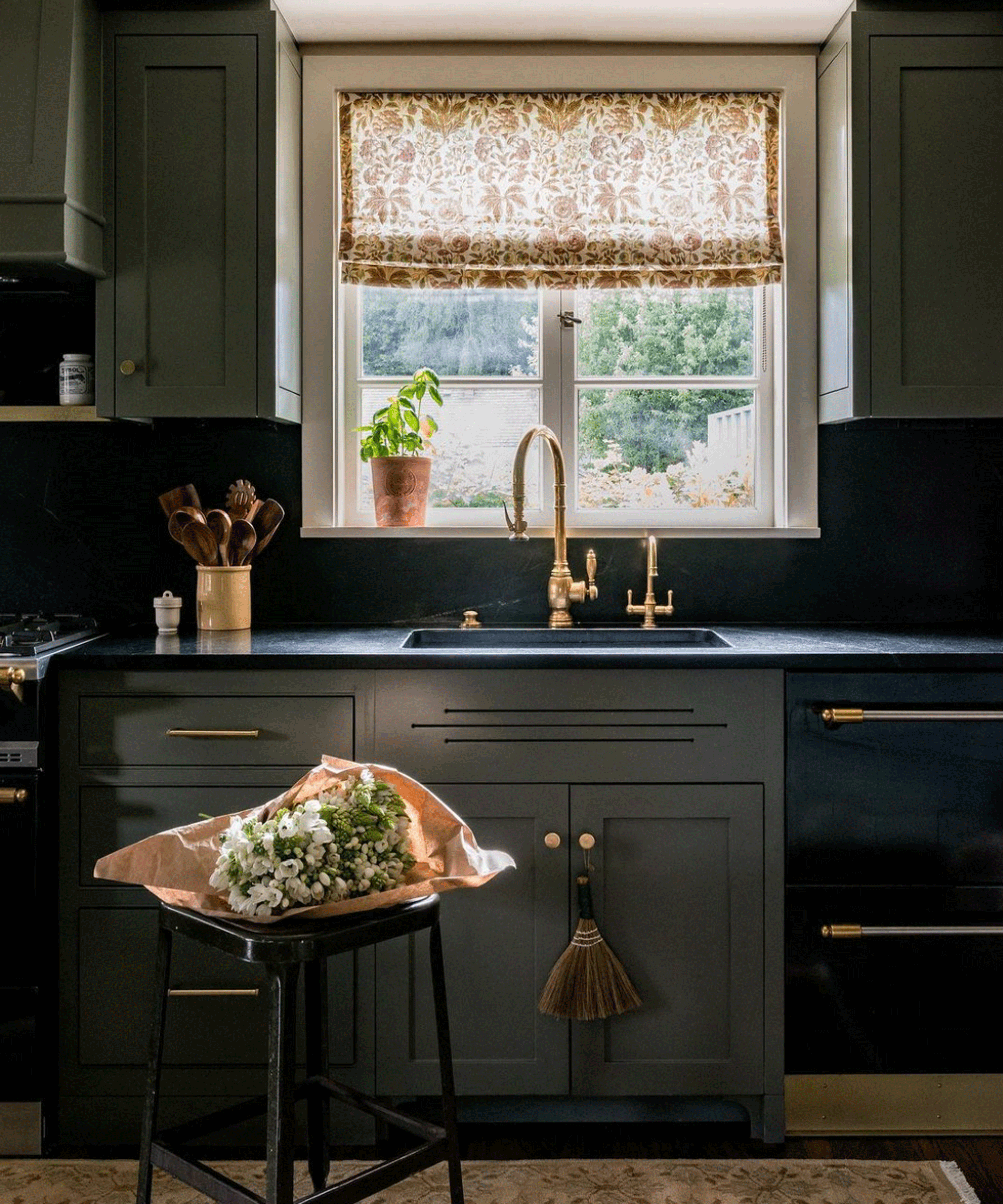 Dark green kitchen and black worktop and splashback along with patterned window blind and rug.