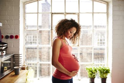 Woman sitting next to window, pregnant with endometriosis, holding baby bump