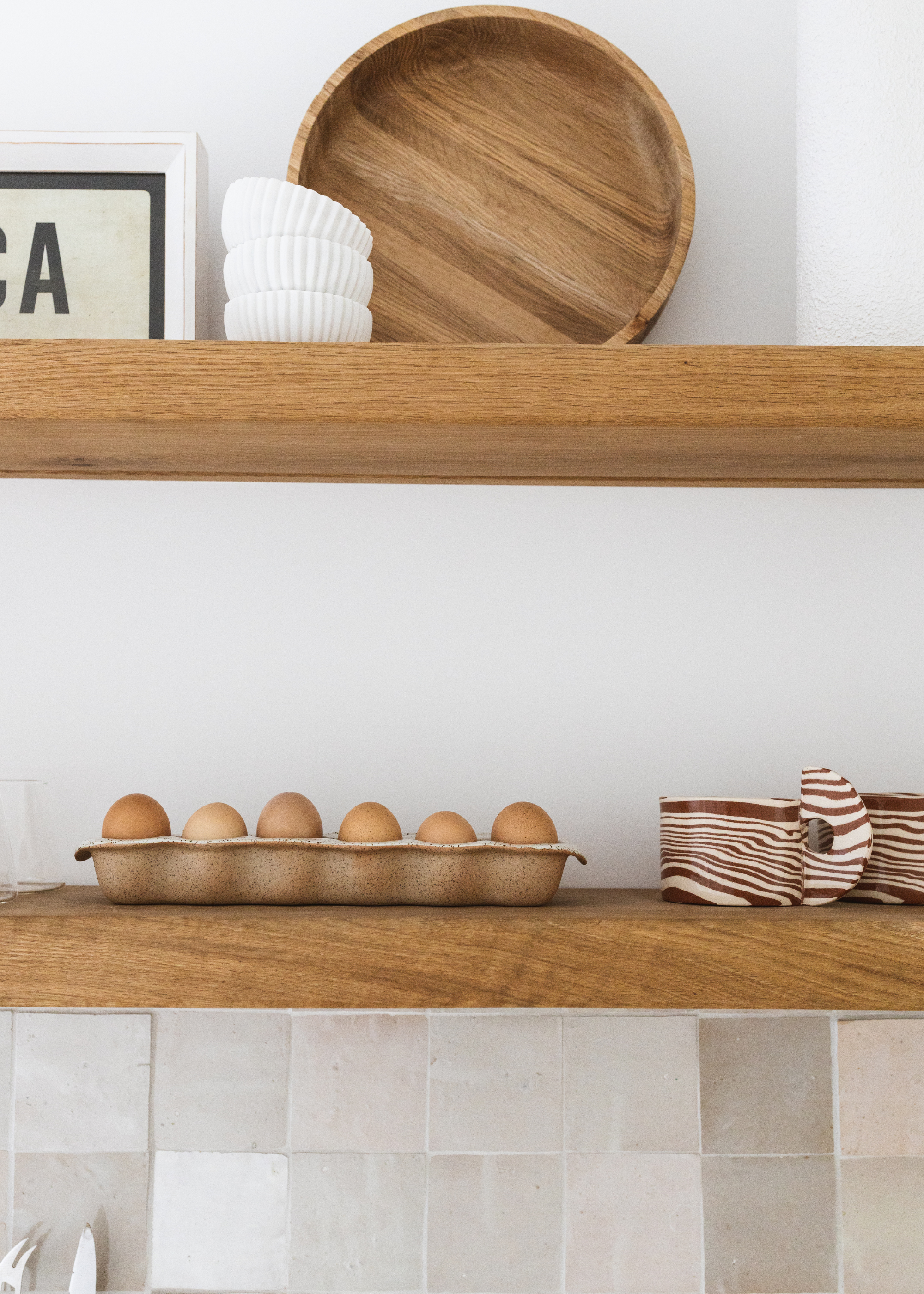 A close-up of kitchen shelves with a crate of eggs, a stack of bowls, textured glasses and a large wooden bowl