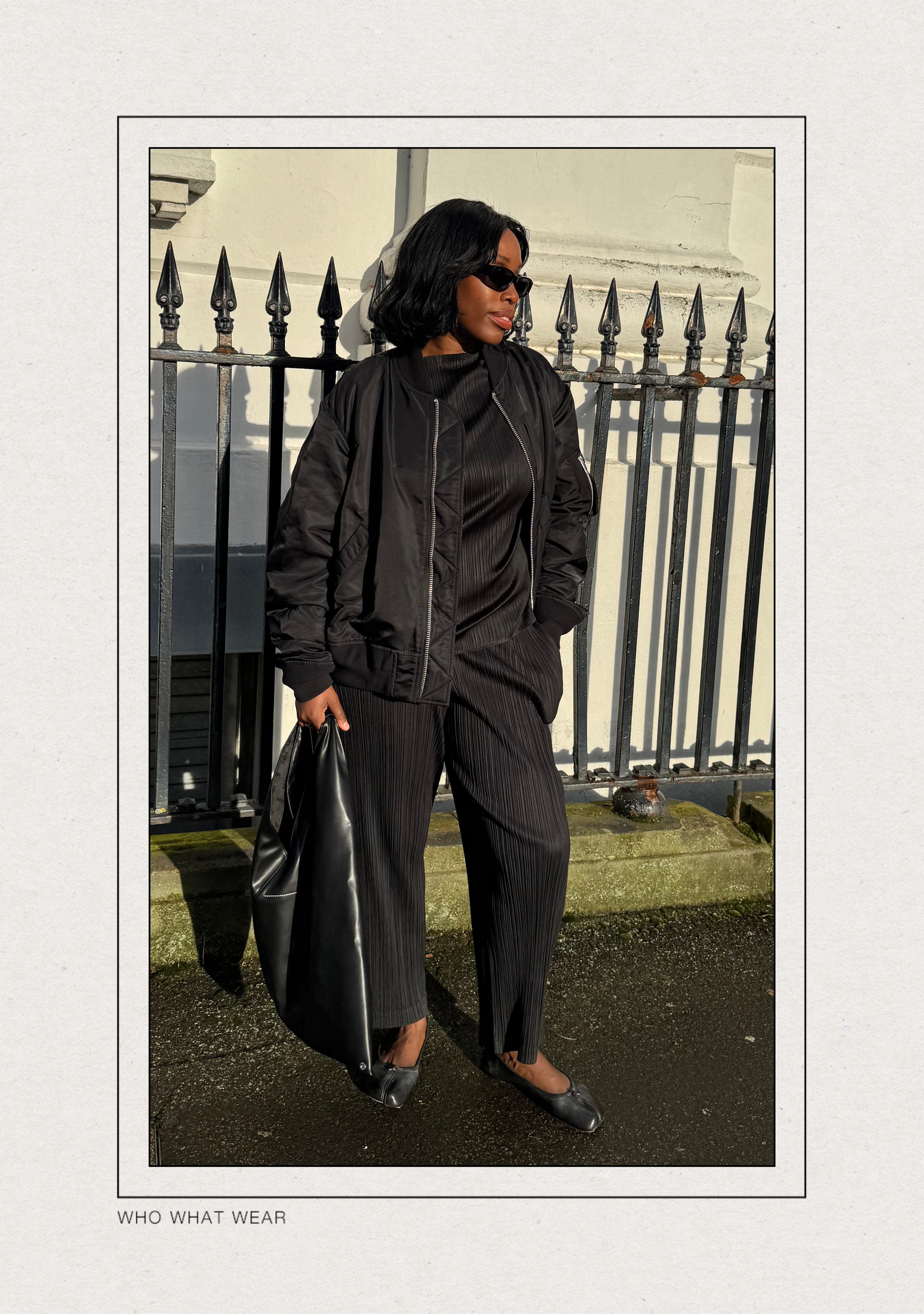 @anuogugbesan wears a black bomber jacket with a Issey Miyake pleated top, matching trousers and Margiela Tabi ballet flats whilst standing in the street