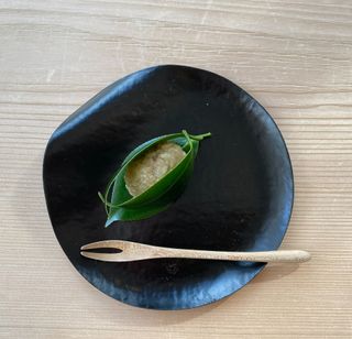 Black plate topped with green leaves on a wooden table with a wooden spoon