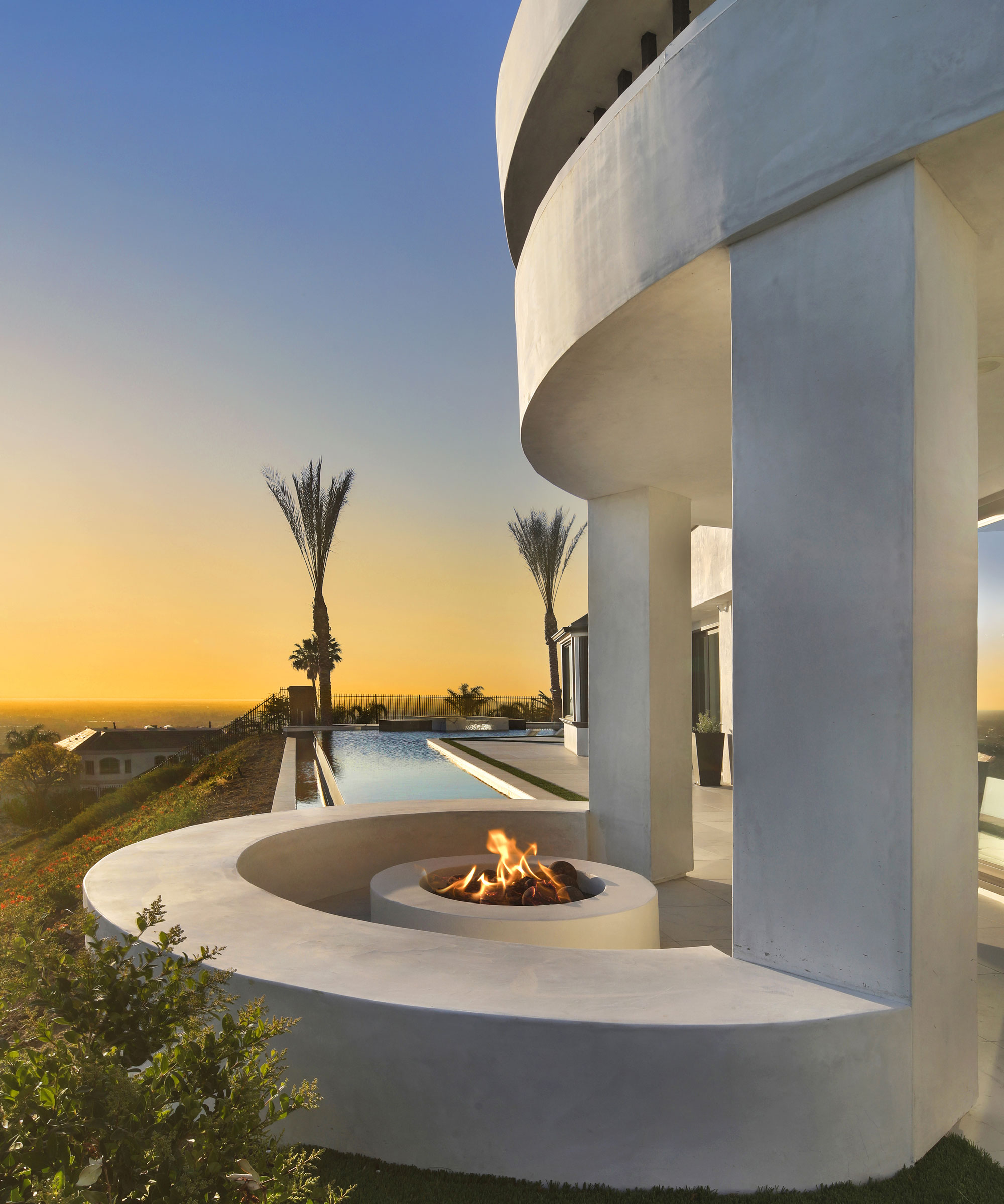 desert modernism landscape design with infinity pool, palm trees, and white sculptured firepit area