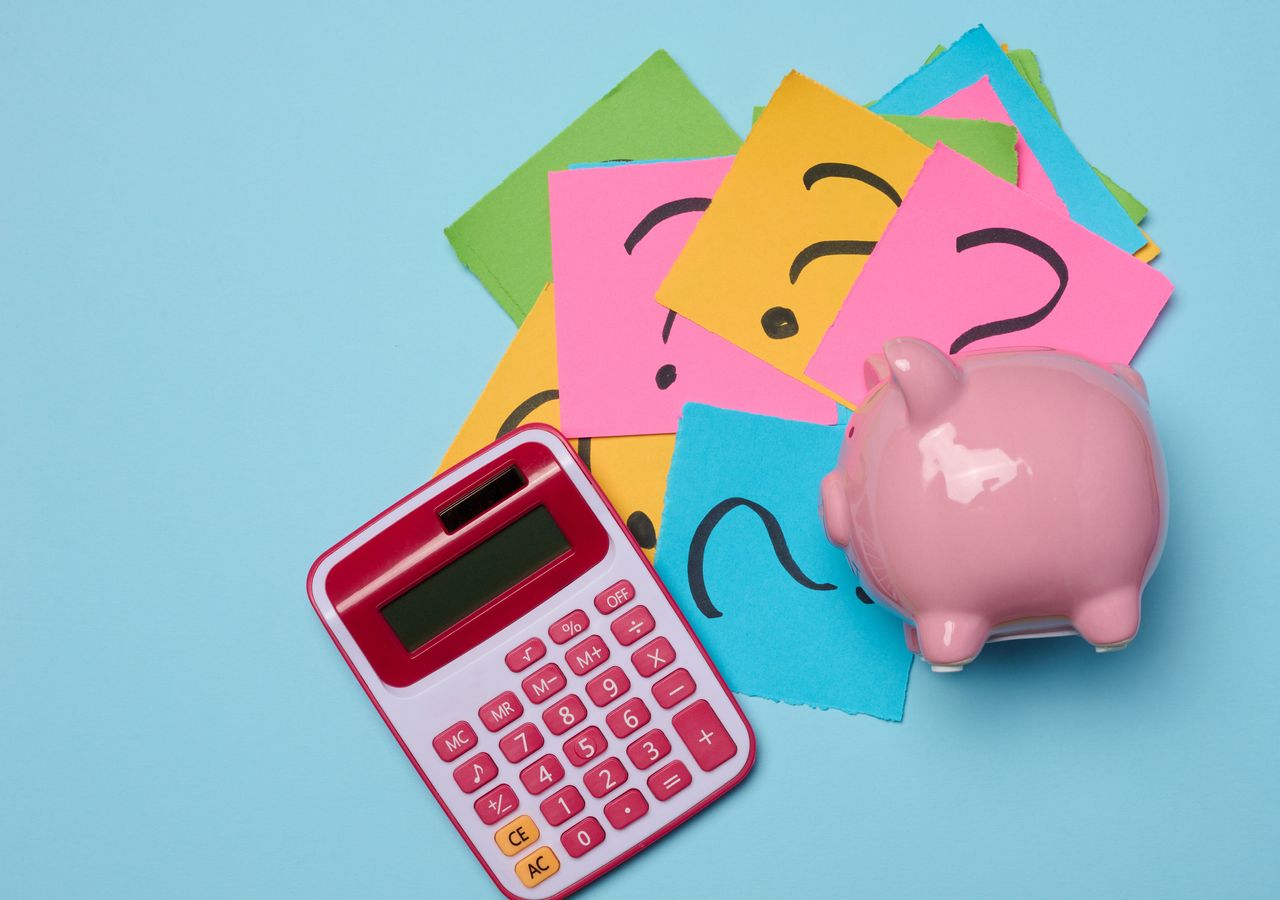 Ceramic piggy bank and sticky notes with drawn question marks on a blue background, top view