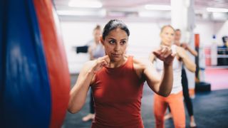 Woman standing with fists raised during cardio boxing class, next to punching bag