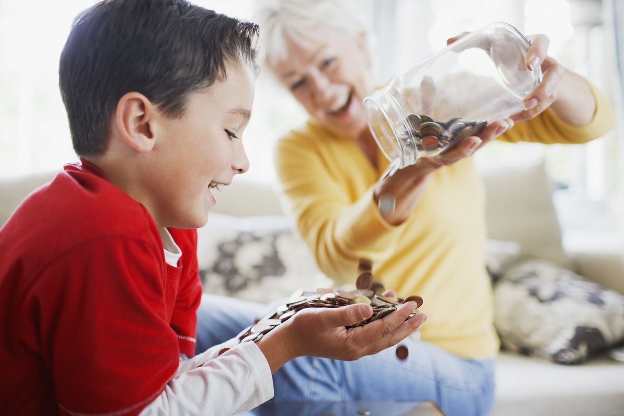 Grandparent tipping a jar of coins into grandchild&#039;s hands