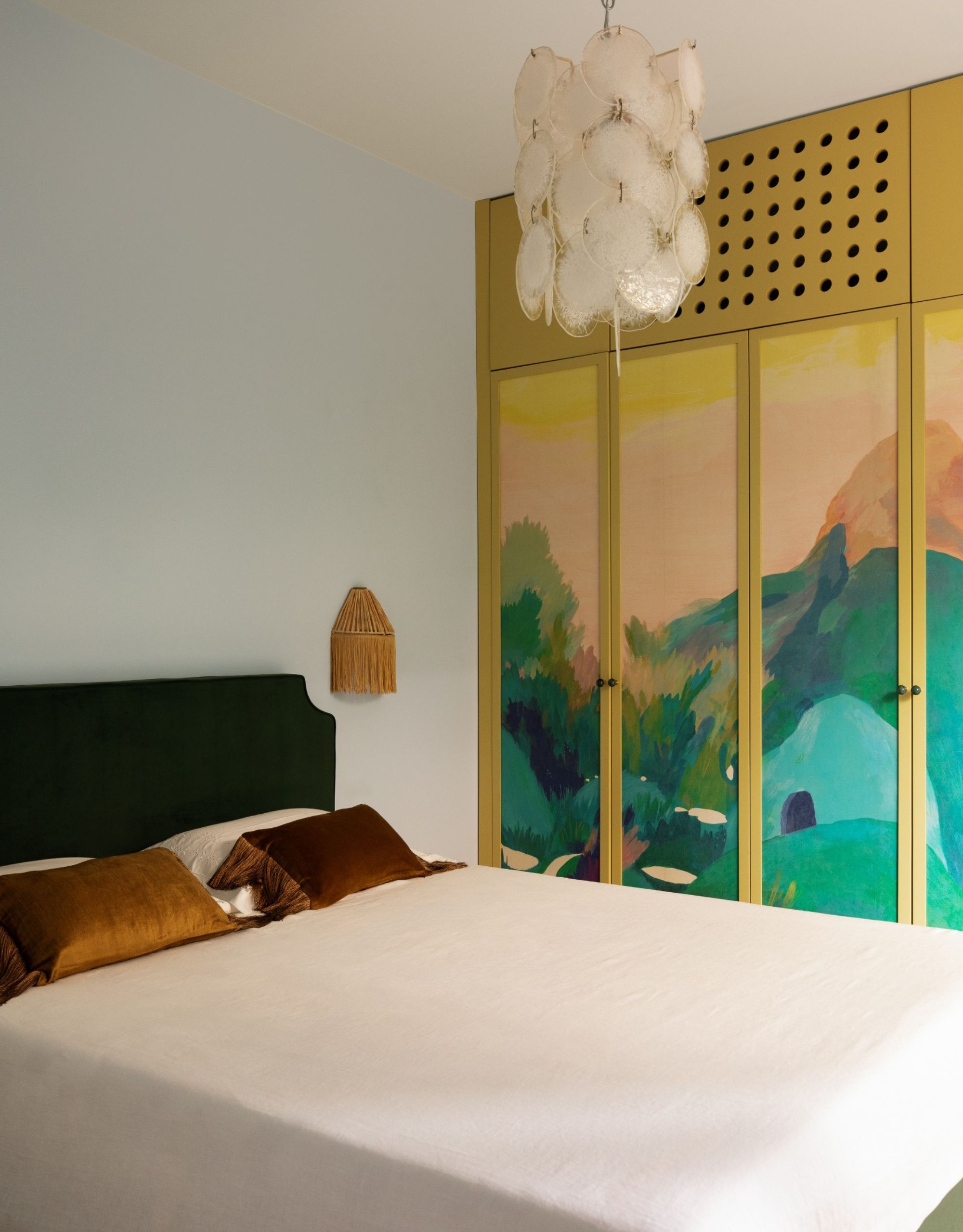 A bedroom with parquet flooring, a simple bed, and a wardrobe painted with a bright wall mural