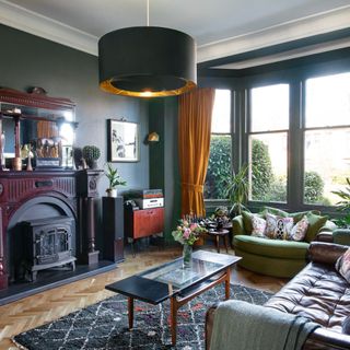Living room with dark teal walls, fireplace and mustard curtains in bay window