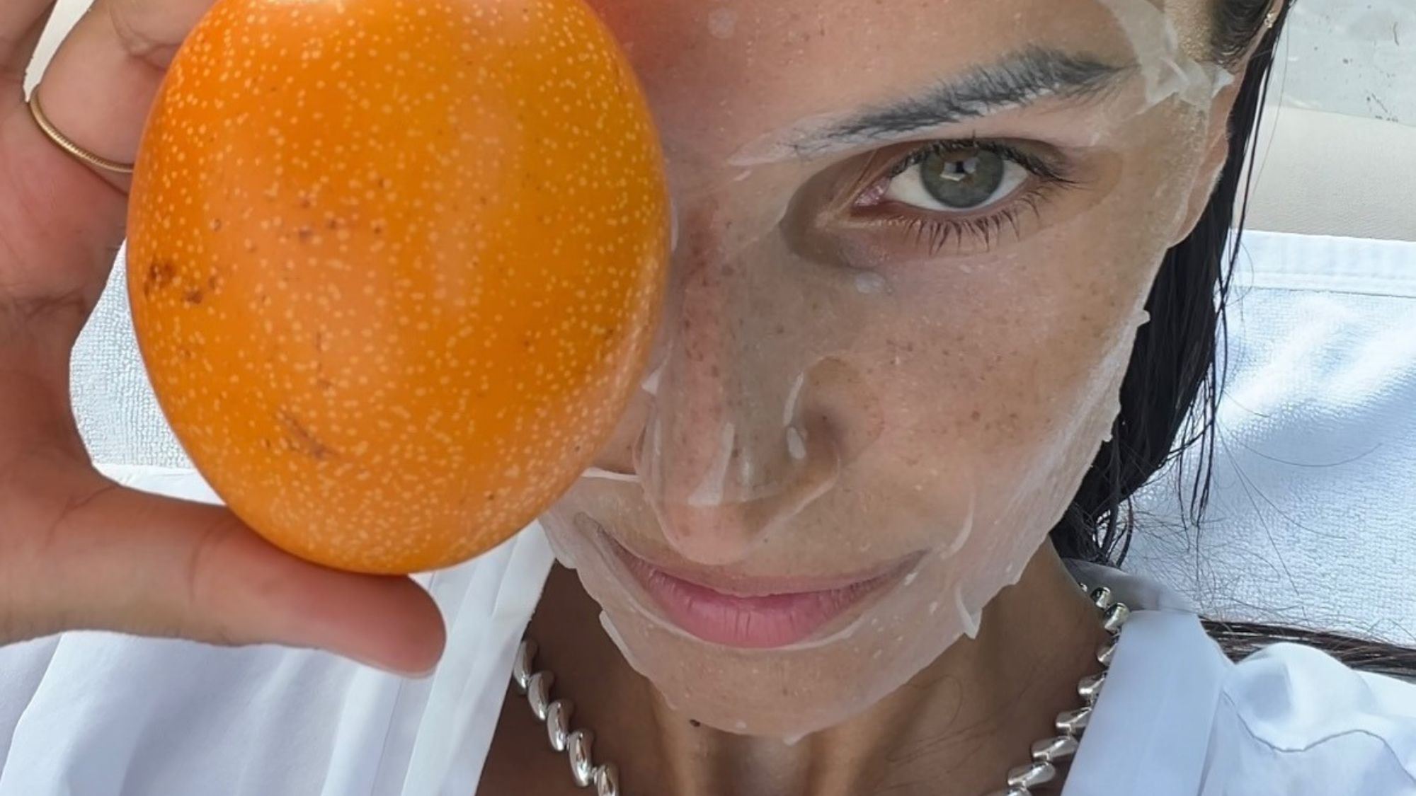 A woman wearing a face mask and holding fruit over her eye.