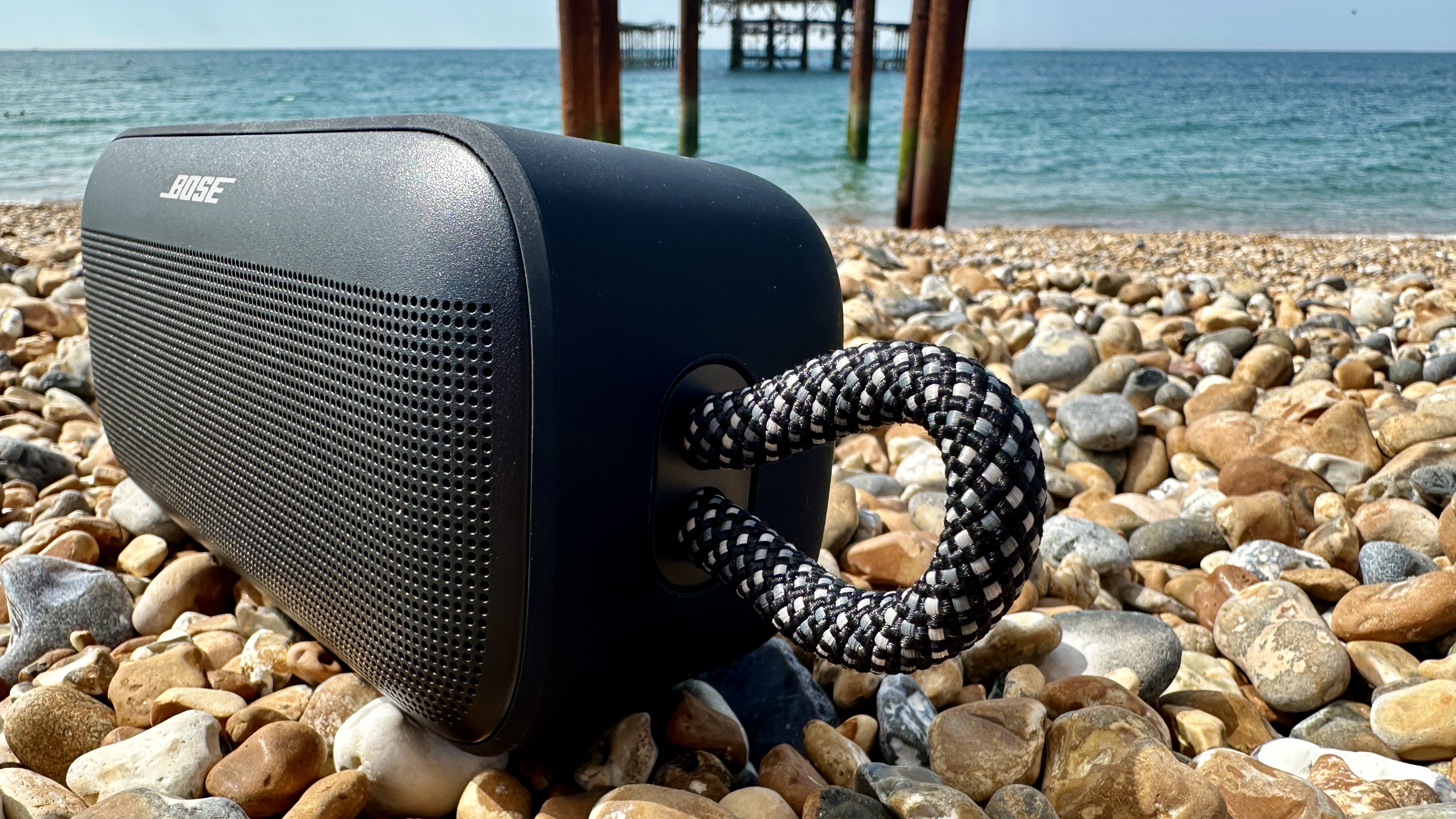 Bose SoundLink Plus on Brighton Beach pebbles, with the old pier in the background
