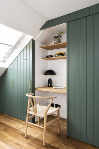 loft closet home office with green panelled sliding door, wooden shelving, wooden chair, wood flooring, white walls
