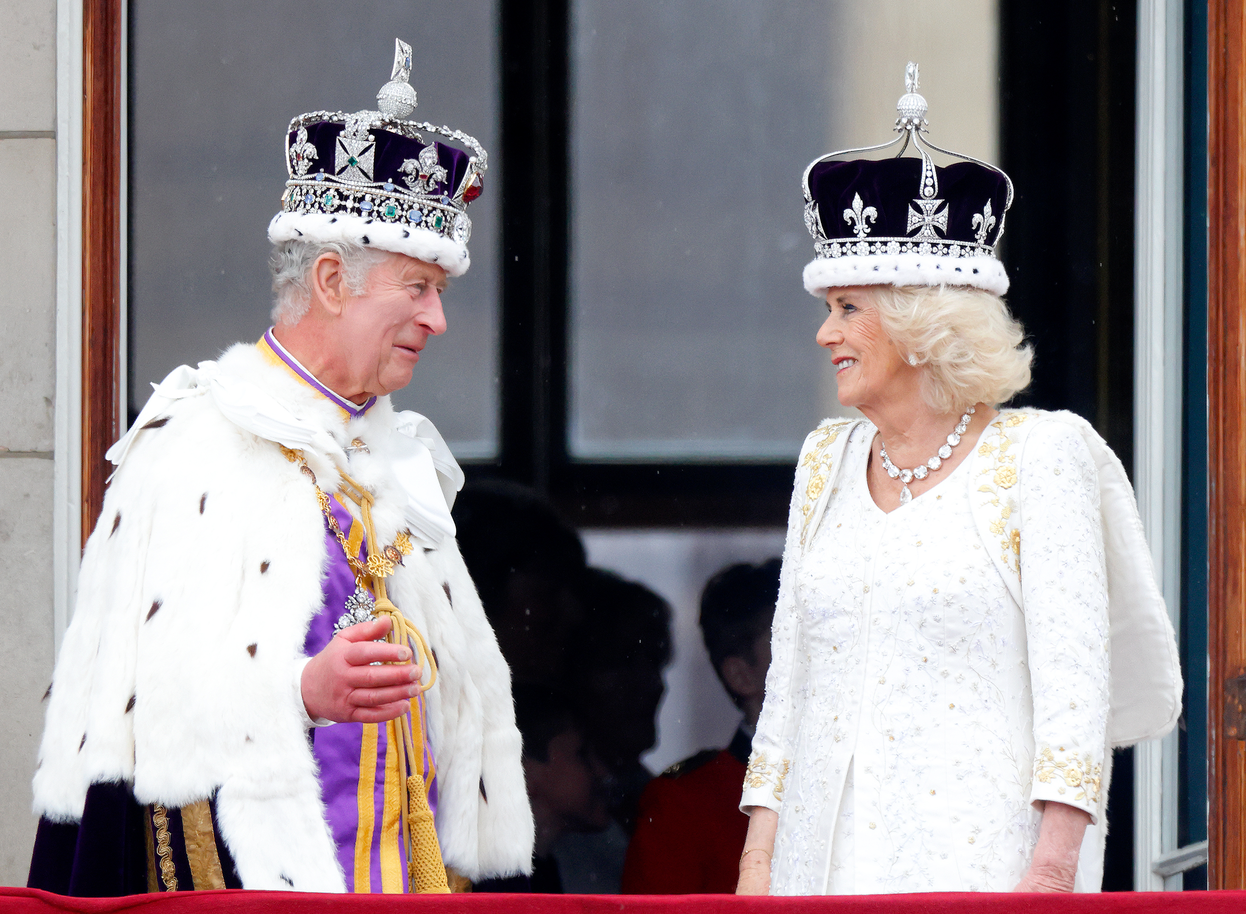 Queen Camilla and King Charles wearing their coronation crowns and outfits smiling at each other