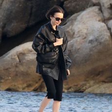 Lilly Collins wearing a black leather jacket, capri pants, and two-tone cream-and-black ballet flats in Mykonos