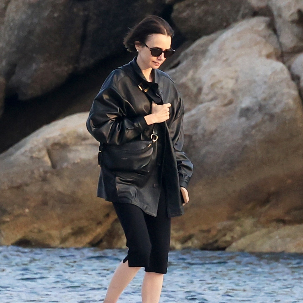 Lilly Collins wearing a black leather jacket, capri pants, and two-tone cream-and-black ballet flats in Mykonos