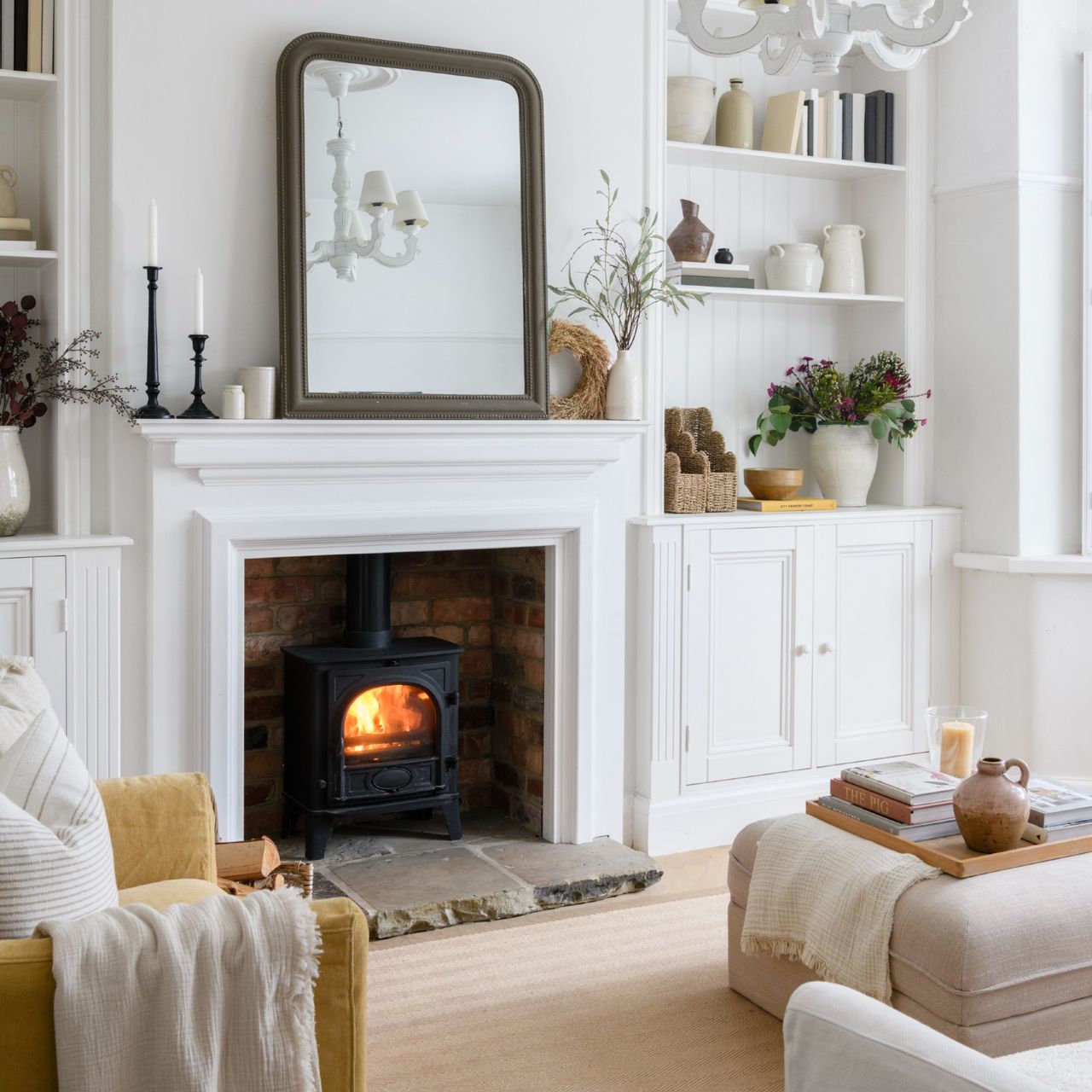 A white living room with a lit wood burning stove placed within a fireplace 