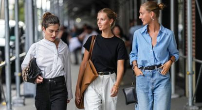 NEW YORK, NEW YORK - SEPTEMBER 13: A guest (L) wears a white striped print pattern shirt, black denim pants, a brown shiny snake print pattern puffy handbag, black denim pants, brown camel shiny leather pointed loafers, a guest (M) gold earrings, a black t-shirt, a camel shiny leather oversized shoulder bag, a black shiny leather belt, gold rings, a gold bracelet, white large pants, flip flop, a guest (R) wears gold earrings, a baby blue shirt, a black shiny leather belt, a black shiny leather zipper clutch, a black watch, silver rings, blue denim large pants, navy blue suede pointed pumps heels shoes , outside COS, during New York Fashion Week, on September 13, 2022 in New York City. (Photo by Edward Berthelot/Getty Images)