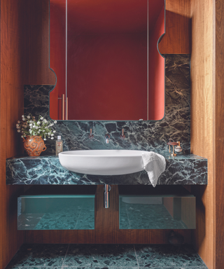 marble cabinet and floor and wall in bathroom with red walls reflected in mirror and wooden panels