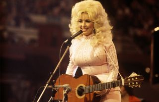 American singer, songwriter and actress Dolly Parton, performs with a guitar, 1976.