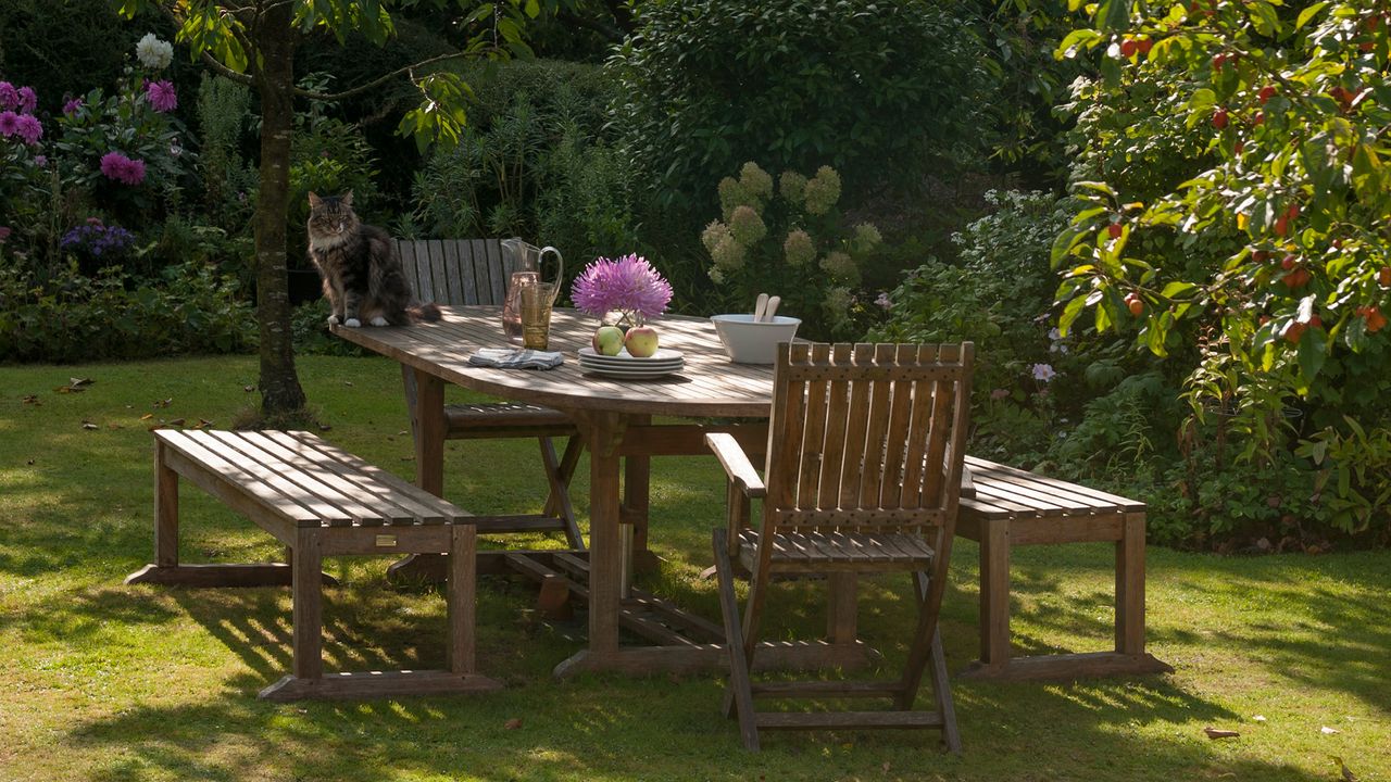 Wooden dining table and chairs on a lush green lawn surrounded by garden borders