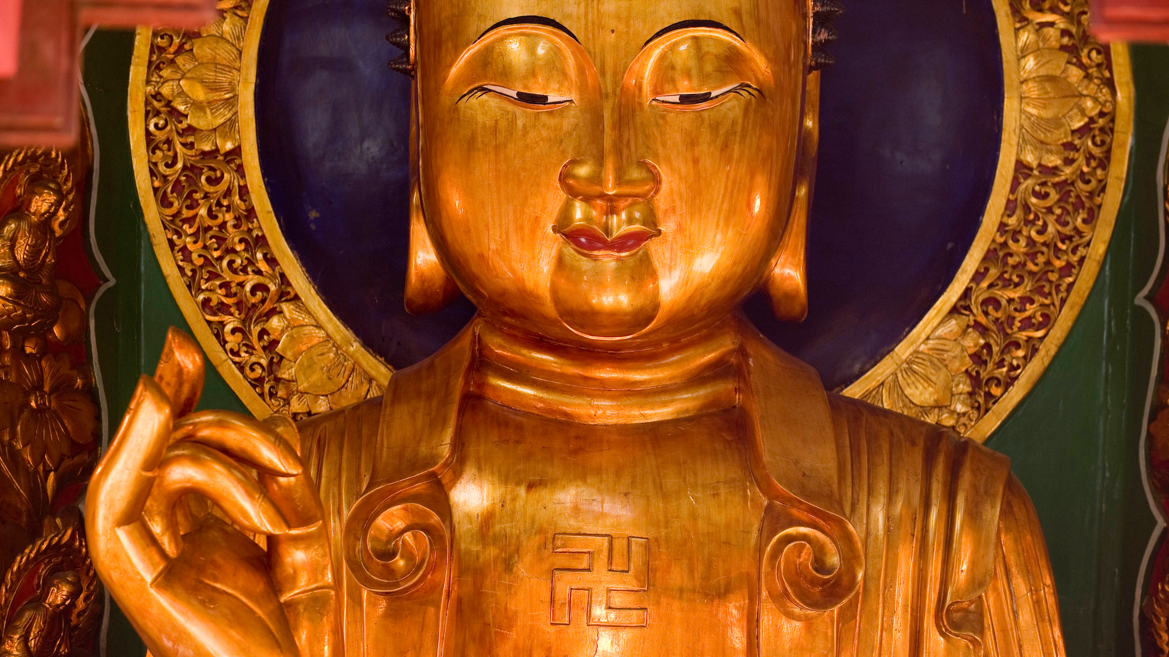 We see a golden statue of Buddha, who has a swastika on his chest.
