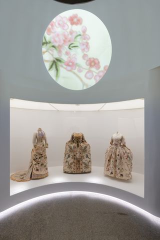 Gallery view of The Met’s Sleeping Beauties Reawakening Fashion, featuring trio of floral dresses in curved room