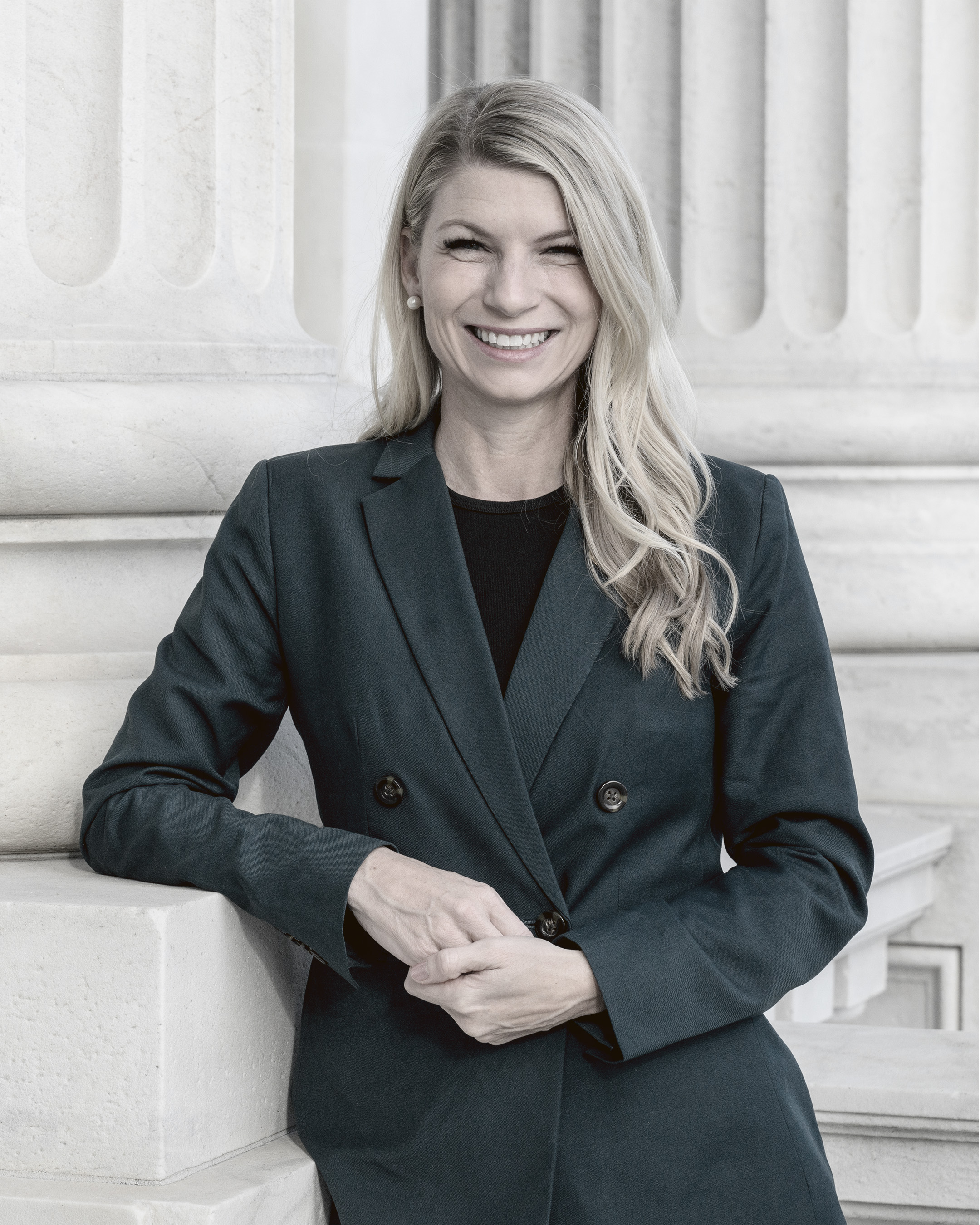 Brittany Pettersen standing in front of white stone columns, smiling in a dark blazer with arms folded.