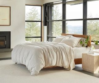 Coyuchi sheets on a bed against a wall covered with floor-to-ceiling windows.