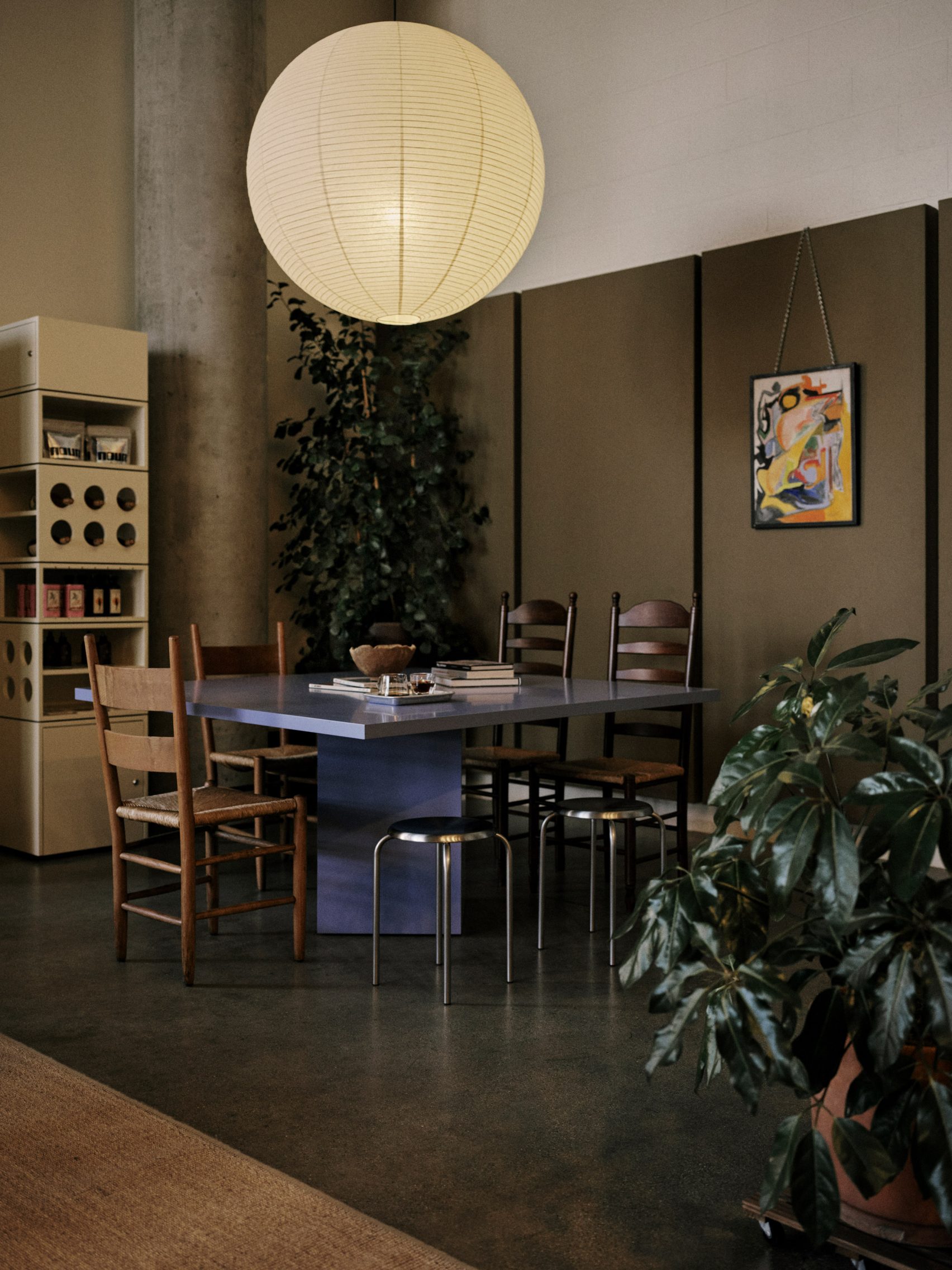 A home-looking coffee shop decorated with modernist furniture including spherical paper lanterns as lights, wood and chrome minimalist furniture, chrome table lamps, and thriving plants.