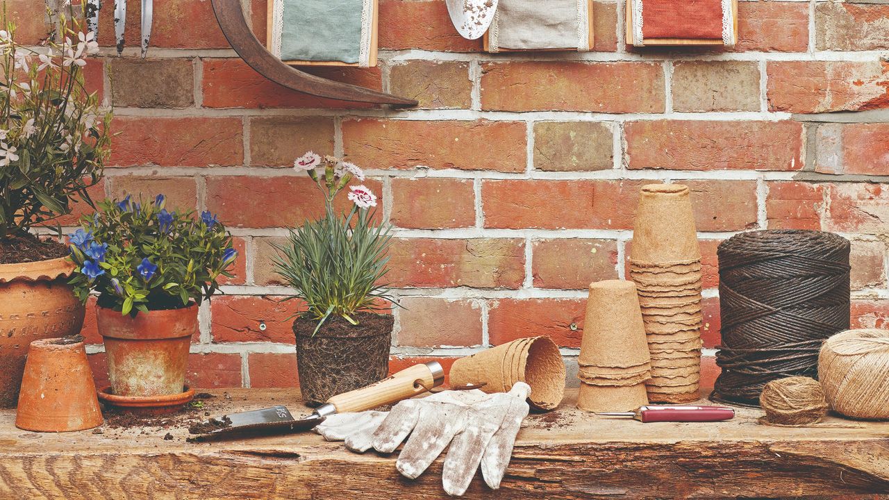 A gardening table against a brick wall with gardening tools and planters