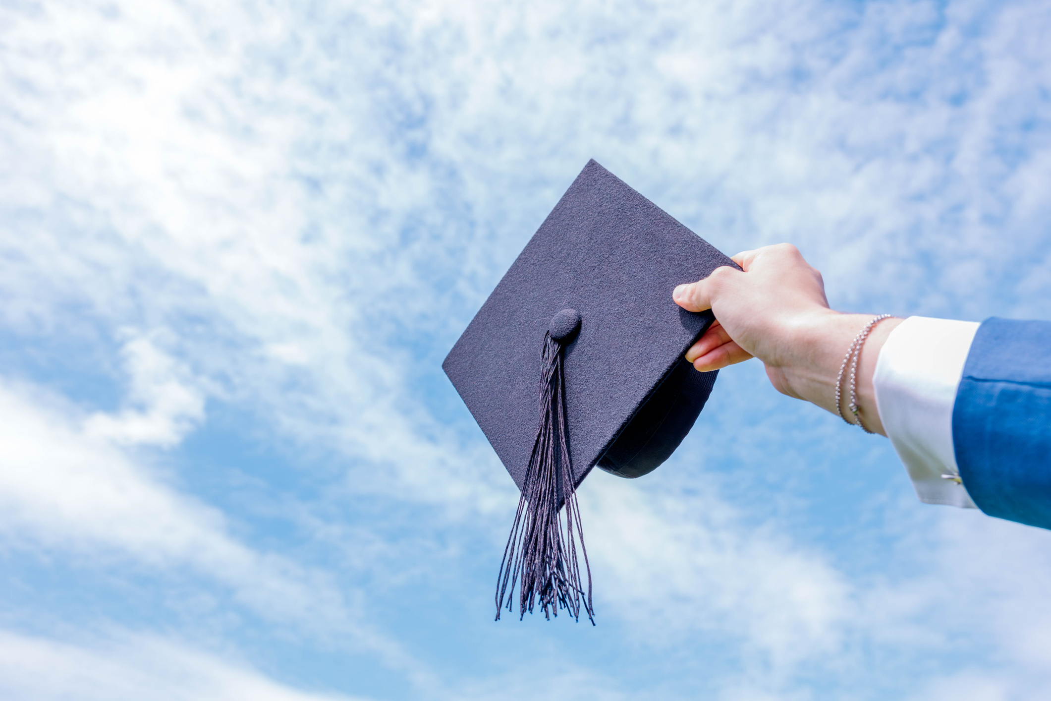 graduation hat being held up by a hand on a blue sky background