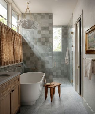 small bathroom with grey zellige tiles a freestanding bathtub wooden vanity and cafe style curtains