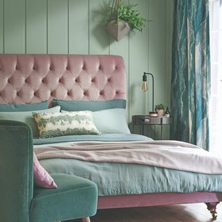 A green-painted bedroom with a bed with a pink quilted fabric headboard