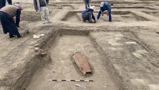 Photographs of a the remains of a 3,500-year-old rest house, marked by rectangular holes in the ground surrounded by people