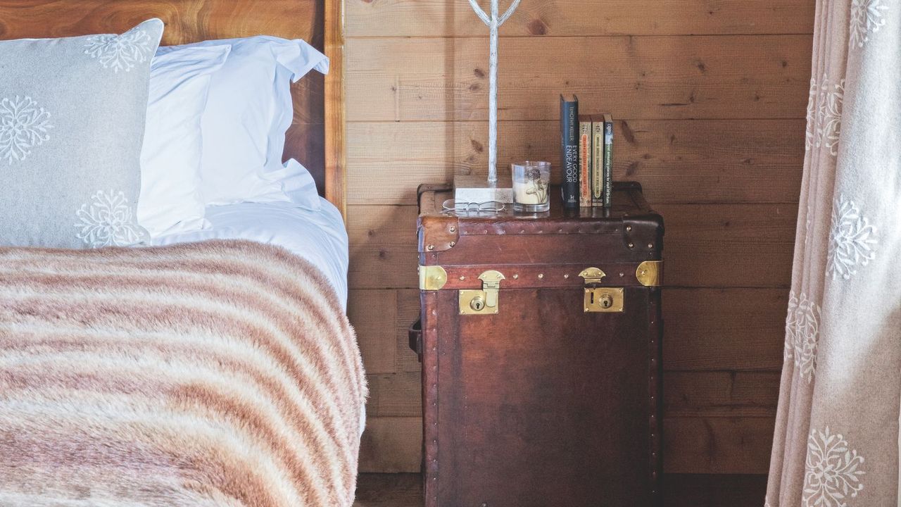 A bed with a faux fur throw and an antique style chest as a bedside table